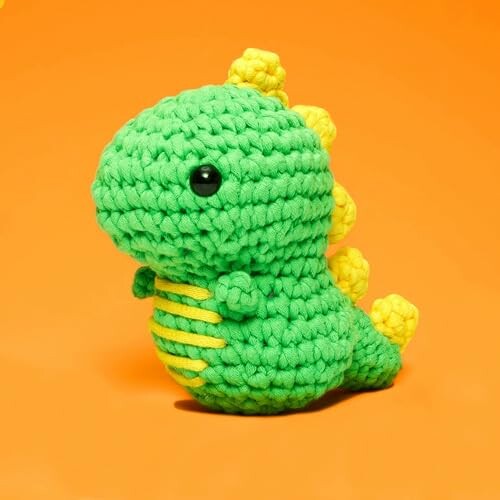 Green crochet dinosaur toy with yellow spikes on orange background